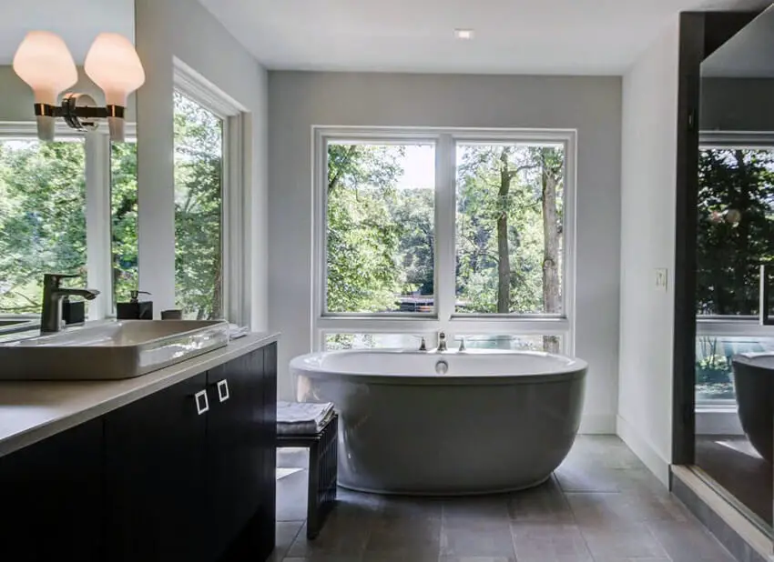 Modern master bathroom with bathtub with window views dark vanity and porcelain tile floors