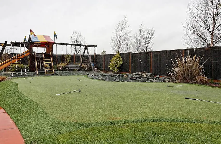 backyard putting green with fake turf surrounded by real grass and water feature pond